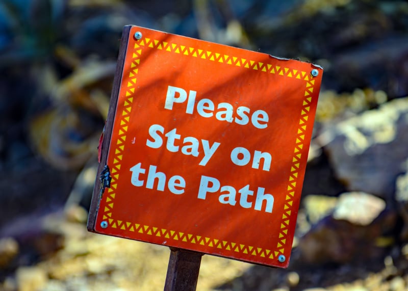 A red sign with please stay on the path on it in white writing.